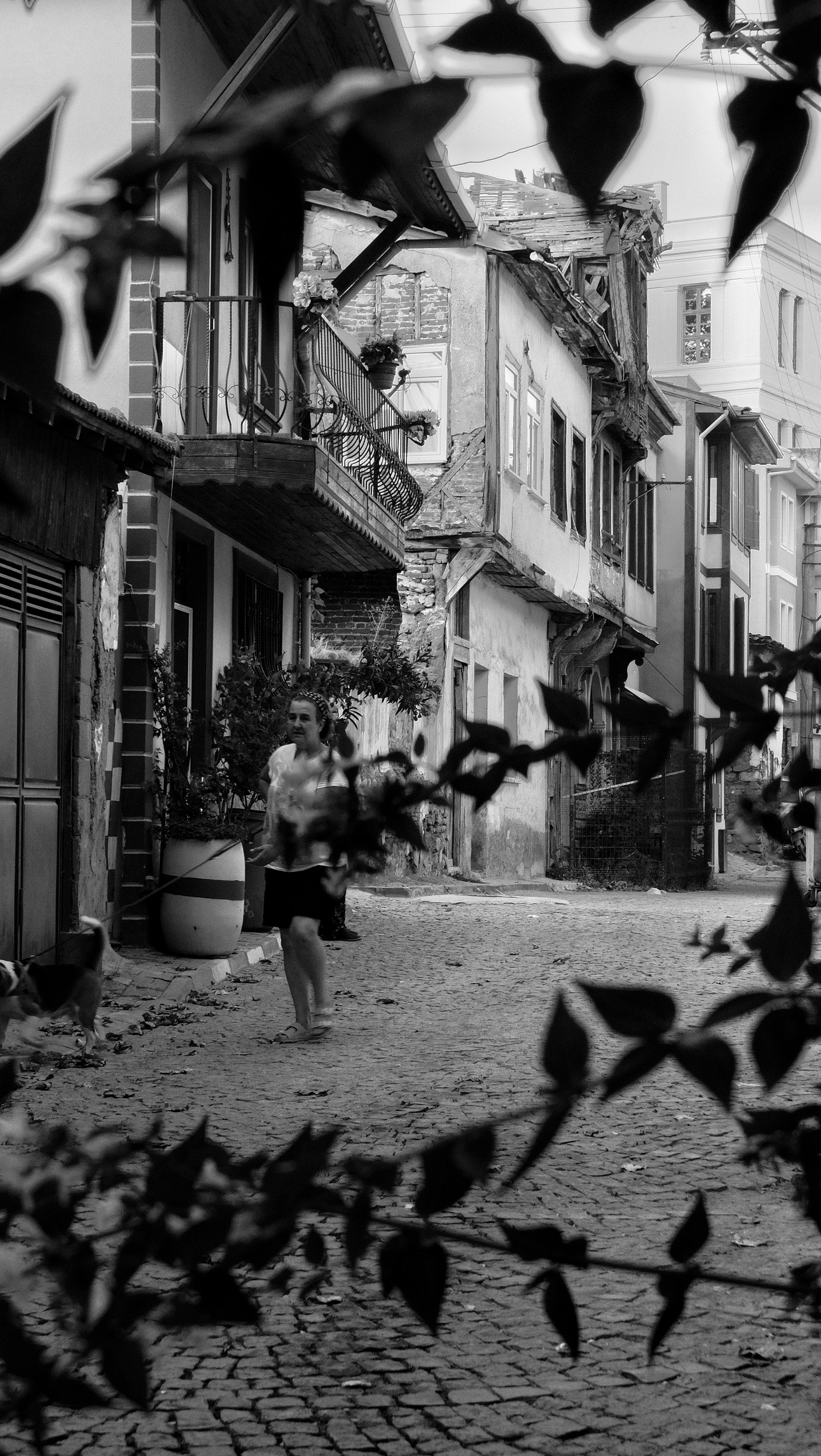 A woman walks down a cobblestone street surrounded by historic architecture in black and white.