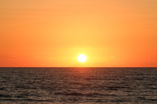 Free Beautiful sunset over a calm ocean with a vibrant orange sky and serene reflection. Stock Photo