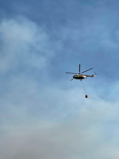Free A helicopter with a water bucket battling a wildfire against a clear blue sky. Stock Photo