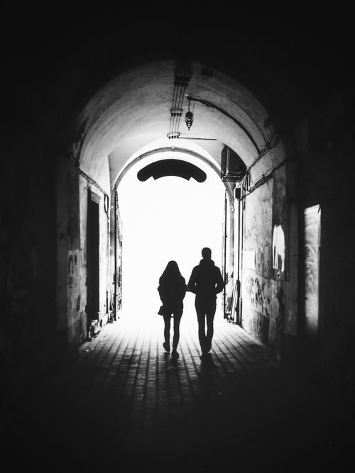 Free Black and white photo of two silhouetted figures walking through an arched tunnel, creating a moody atmosphere. Stock Photo