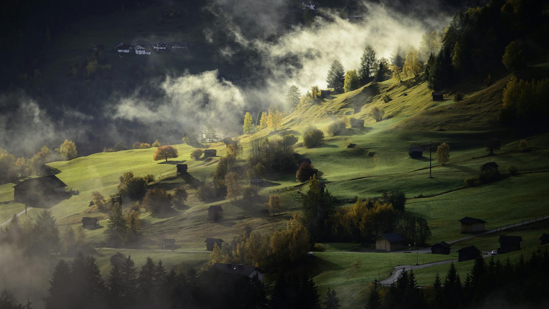 Scenic view of a misty hillside landscape with scattered cabins in autumn light.