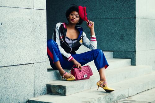 Free Stylish woman in vibrant outfit poses on concrete steps with a red handbag in an urban setting. Stock Photo