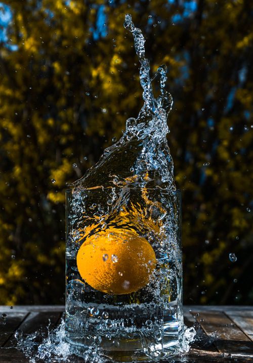 Free A vibrant orange splashing into a clear glass of water outdoors, captured in mid-air, showcasing motion and freshness. Stock Photo