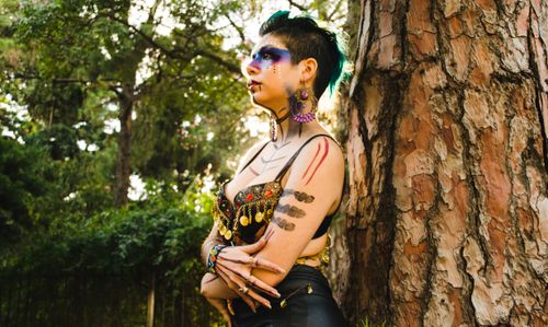 Free A vibrant portrait of a woman in elaborate makeup and fashion against tree bark outdoors. Stock Photo