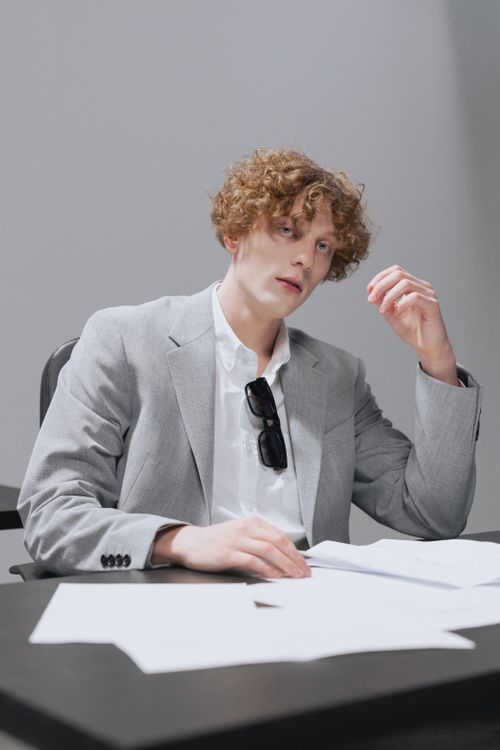 Free Curly-haired employee in a gray suit working with paper documents at a desk. Stock Photo