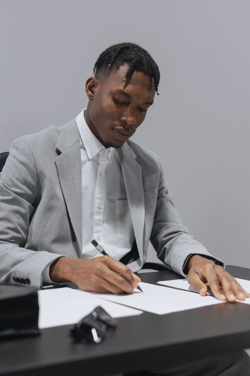 Free Focused businessman in a gray suit writing at his desk. Professional office setting. Stock Photo