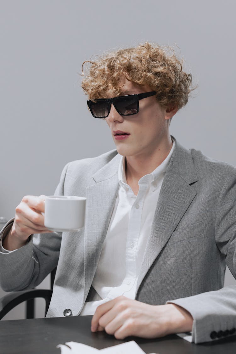 A Man In Gray Suit Wearing Sunglasses While Holding A Cup Of Coffee