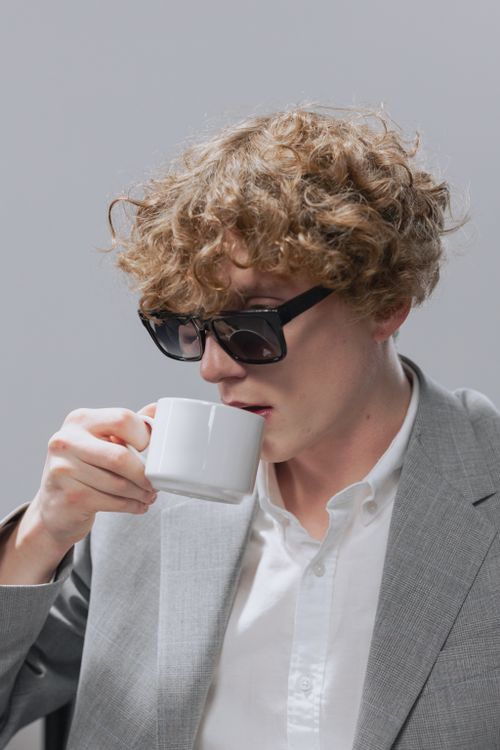 Free A business professional with curly hair sipping coffee in a gray suit and sunglasses. Stock Photo