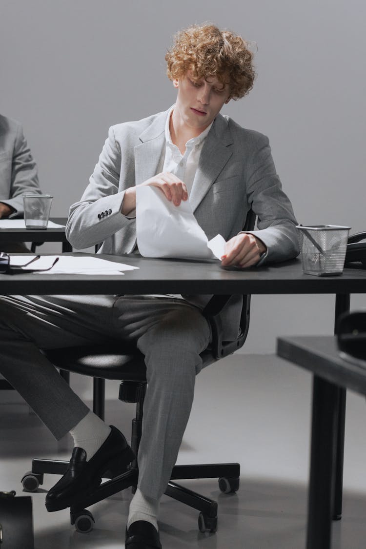 A Man In Gray Suit Sitting On The Chair While Tearing A Paper