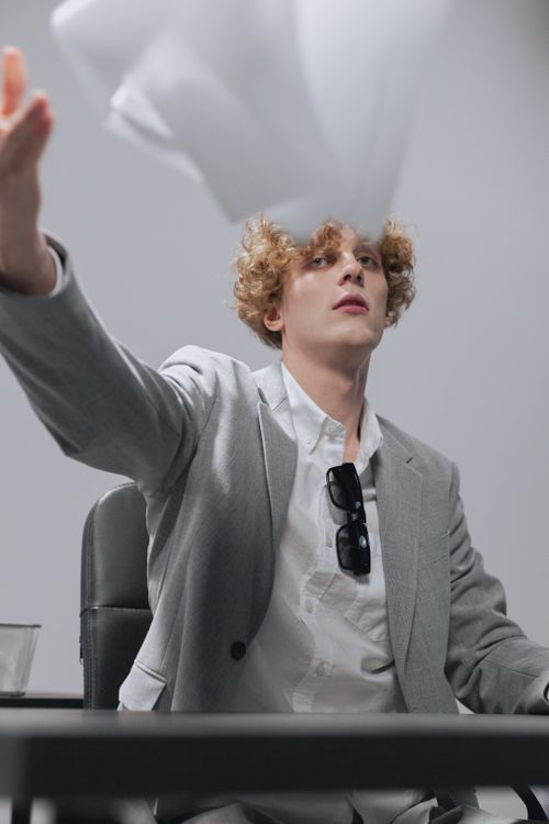 Free Caucasian man in a suit playfully tossing papers in a modern office setting. Stock Photo