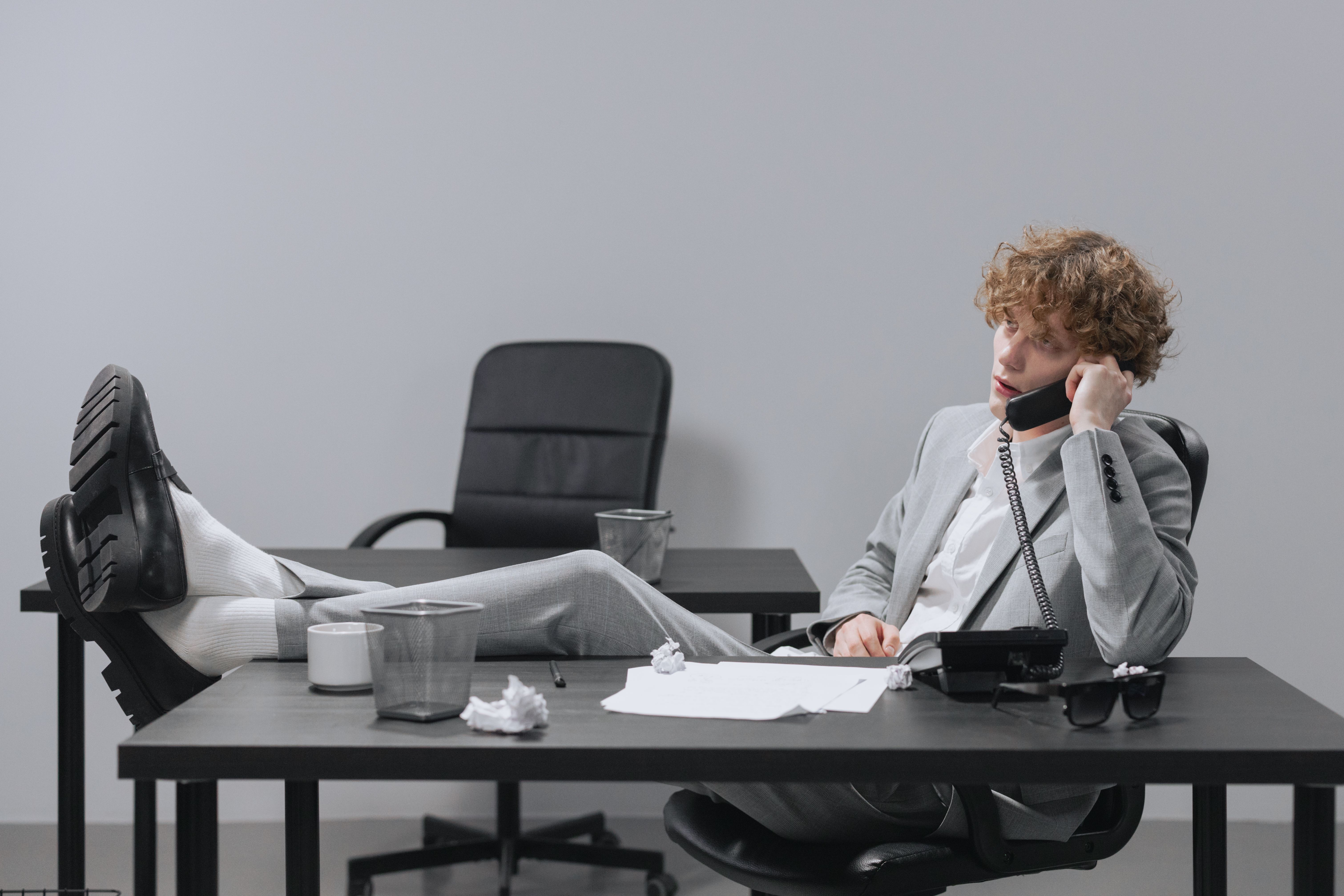 a man in gray suit sitting on the chair while talking on the phone