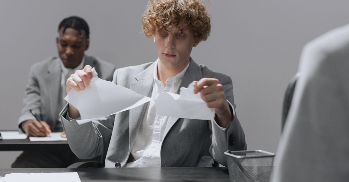 Dos empleados en trajes sentados en escritorios, uno rompiendo papel.