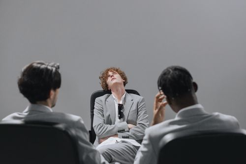 Free Three professionals in a gray conference room, two facing away, one appearing relaxed. Stock Photo