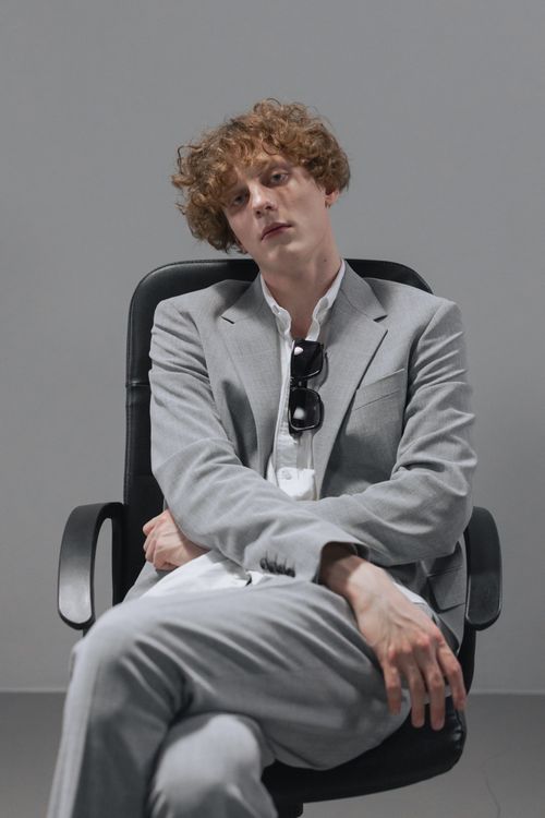 Free A young redhead businessman in a gray suit sits thoughtfully on an office chair. Stock Photo
