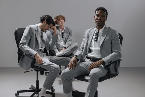 Free Three young men in gray suits posing confidently in a studio setting. Stock Photo