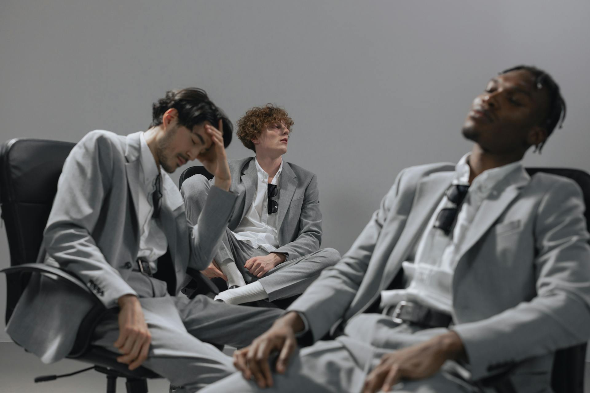 A diverse group of office workers in gray suits sitting relaxed in chairs indoors.