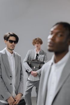 Group of fashionable men posing in grey suits with a briefcase in a studio setting.