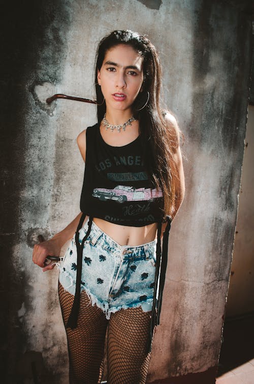 Frau Trägt Ein Schwarzes Grafisches Crop Top Aus Los Angeles, Stonewashed Cut Off Shorts Aus Blauem Denim Und Schwarze Netzstrümpfe