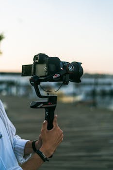 Hands holding a camera mounted on a gimbal, showcasing videography equipment outdoors.