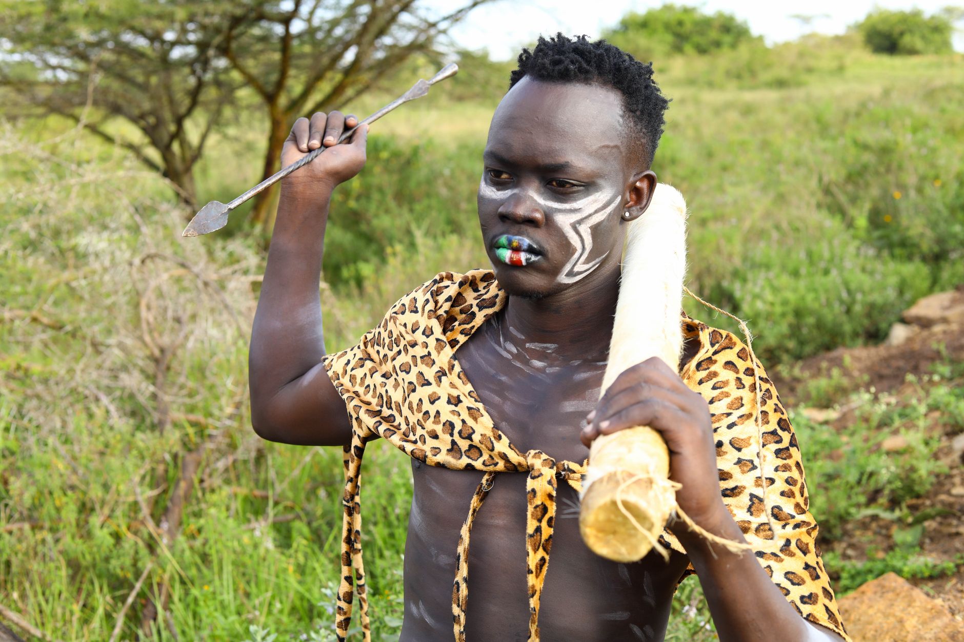 A tribal man in traditional attire with body paint and an arrow in a natural landscape.