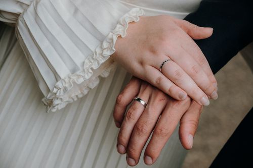 Free Close-up of a couple holding hands, featuring wedding rings and elegant attire, signifying love and union. Stock Photo