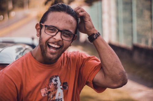 Free A joyful man wearing glasses smiles in an urban outdoor setting, exuding positivity and style. Stock Photo