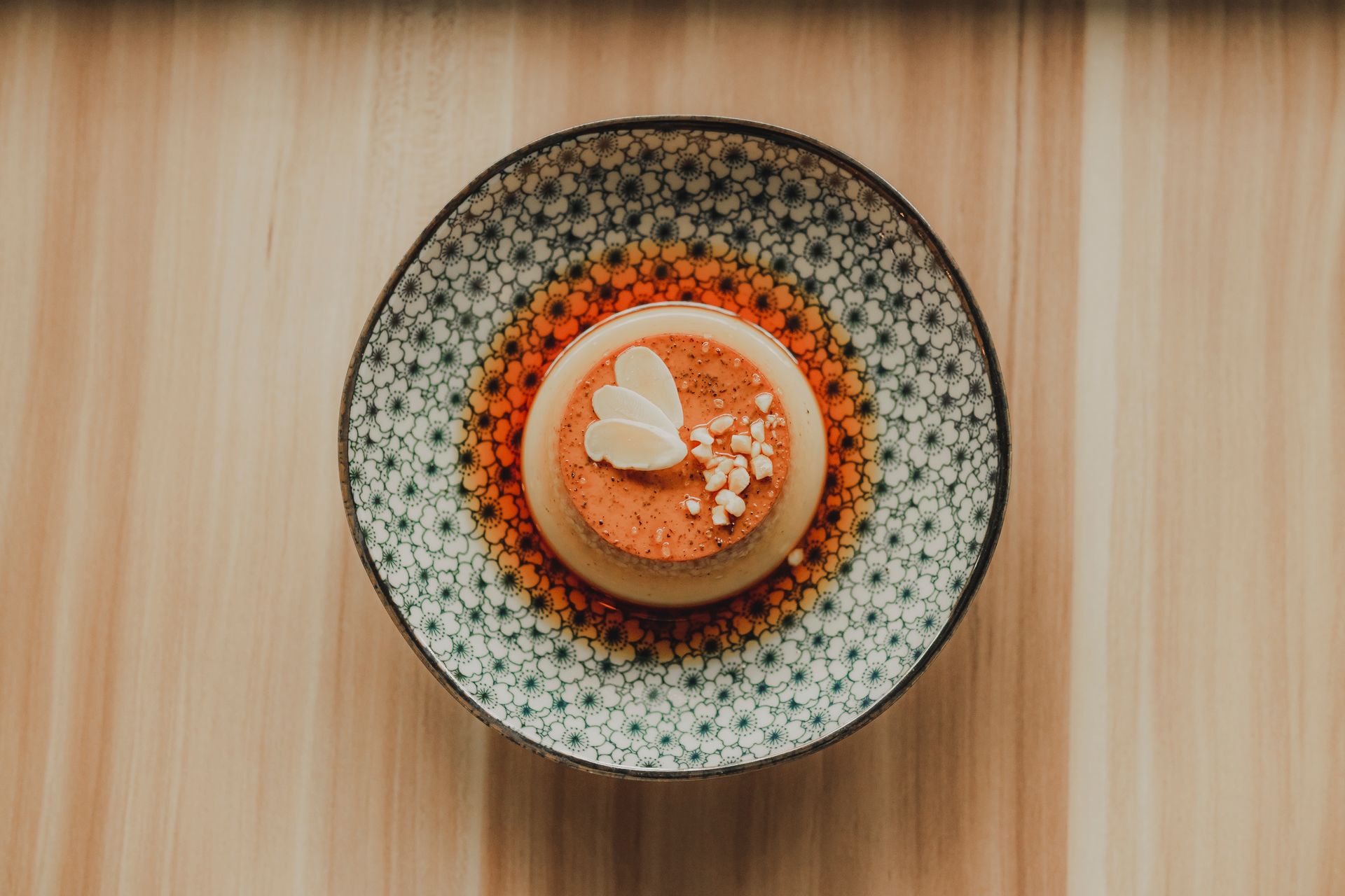 A beautifully presented flan dessert served on a decorative plate with a wooden background.
