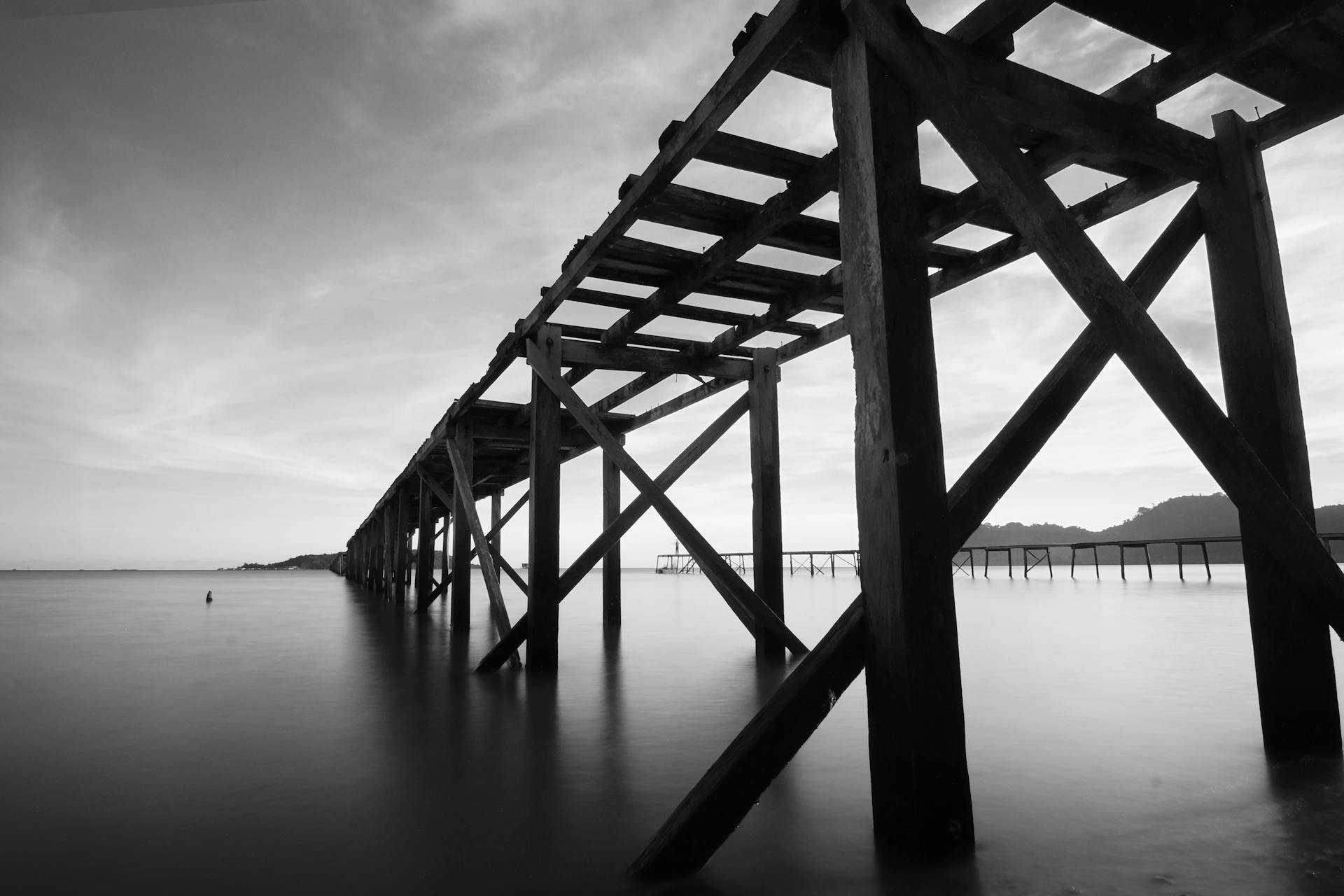 Black and white image of a wooden pier stretching into the sea in Semporna, Malaysia.