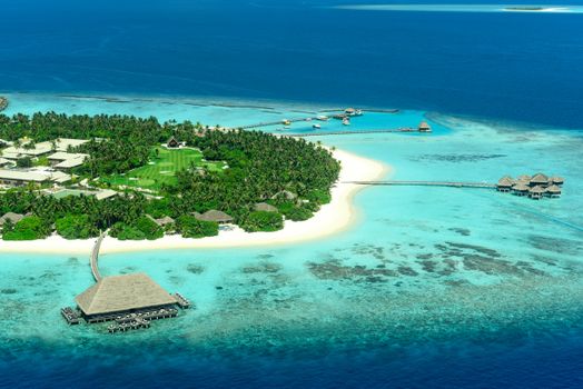 Stunning aerial view of a tropical island resort in the Maldives with crystal clear waters and lush greenery.