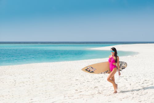 Free A Sexy Woman in Pink Swimsuit Walking at the Beach while Holding a Surfboard Stock Photo
