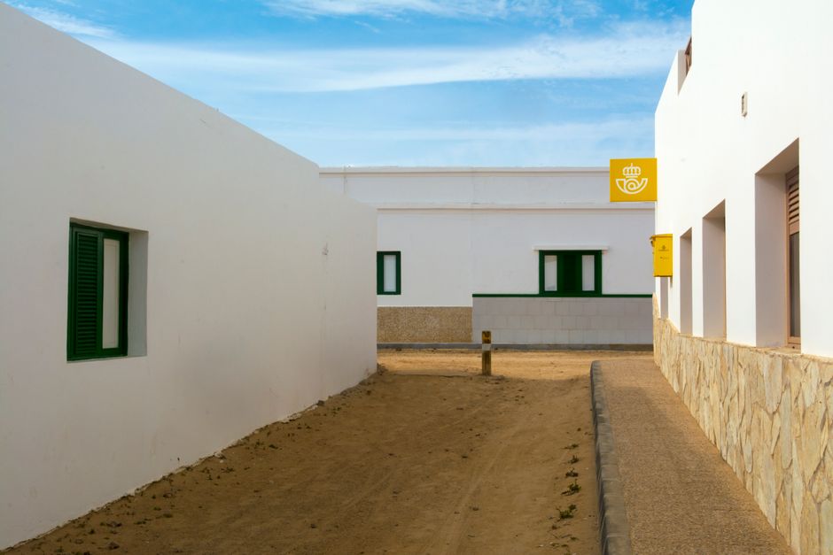 Encantador camino de aldea entre edificios blancos que conduce a una oficina de correos.