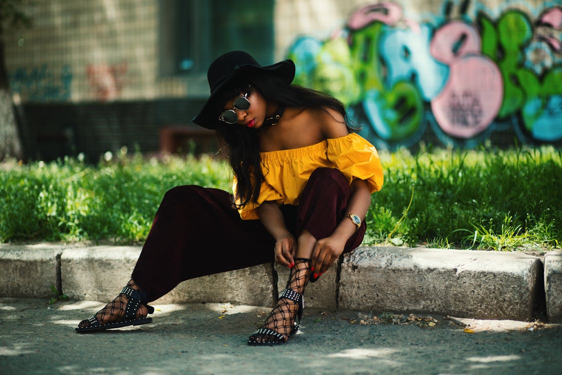 Woman Wearing Yellow Off-shoulder Top and Black Pants Sitting on Sidewalk Fixing  Lace Sandals · Free Stock Photo