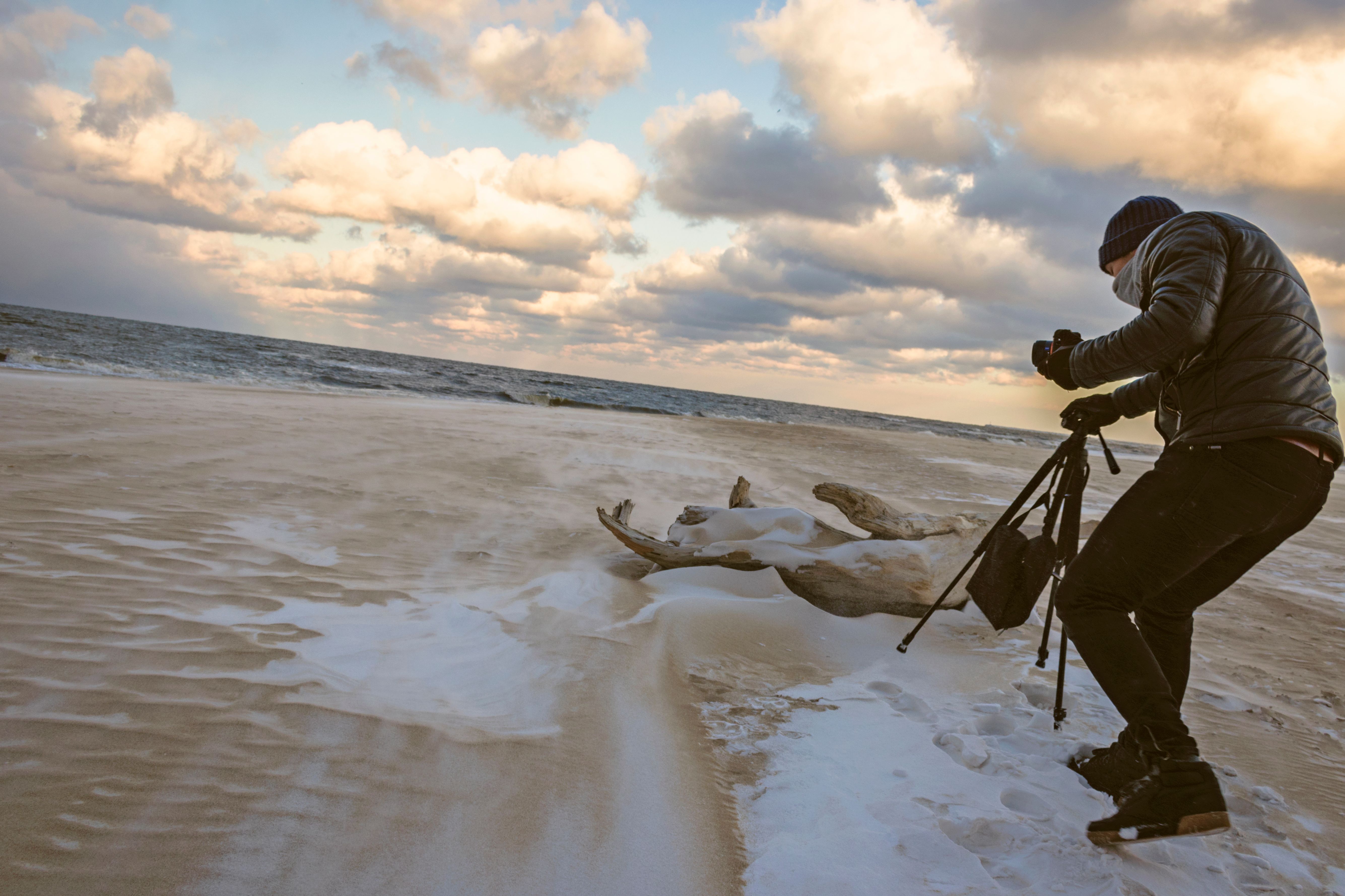 A photographer capturing a scenic beach landscape during sunset with dramatic clouds.