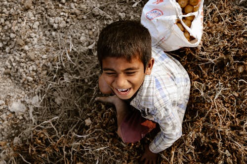 Free High-Angle Shot of a Boy Laughing while Sitting on the Ground Stock Photo
