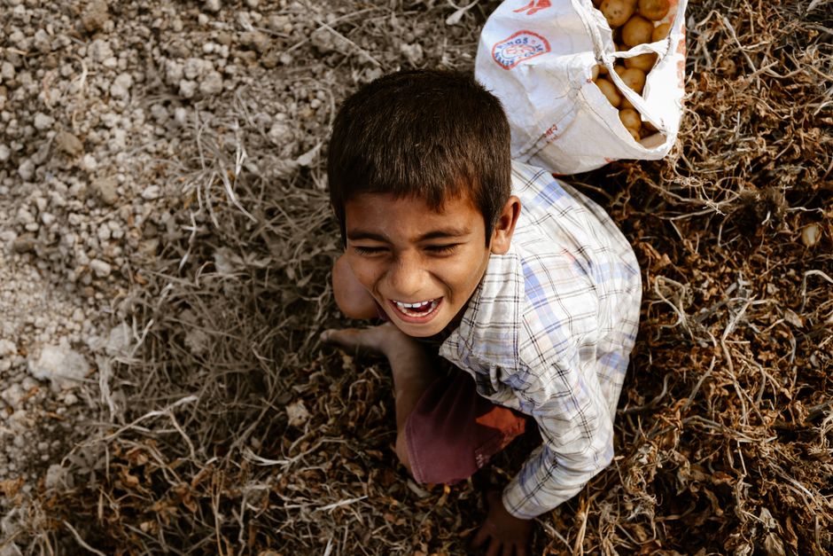 Niño del sur de Asia riendo en un campo de patatas, al aire libre en Bangladesh.