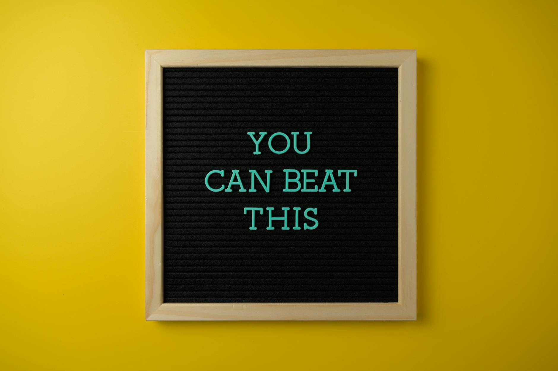 Black letter board with motivational phrase 'You Can Beat This' on vibrant yellow background.