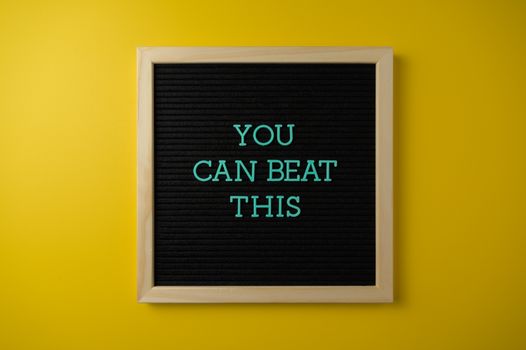 Black letter board with motivational phrase 'You Can Beat This' on vibrant yellow background.