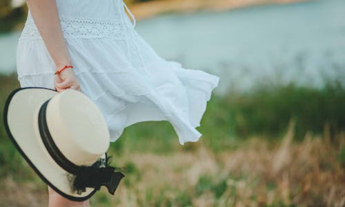 Woman in White Dress Holding White and Black Hat at Daytime