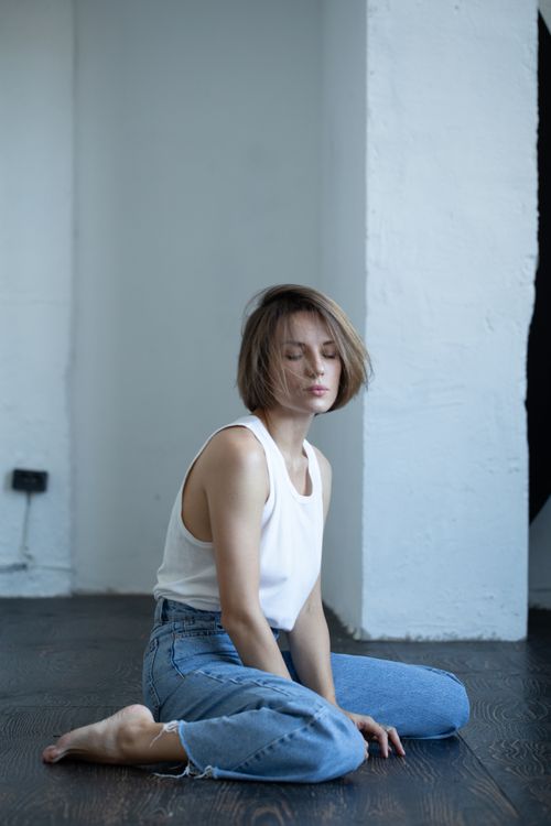 Free A peaceful scene of a woman with short hair, eyes closed, wearing a casual outfit, sitting on the floor indoors. Stock Photo