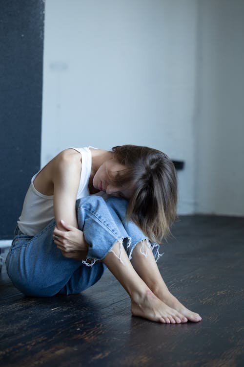 Woman in White Tank Top and Blue Denim Jeans Sitting on Floor