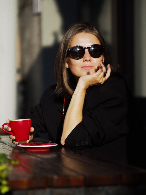 Free Stylish woman in sunglasses enjoying coffee outdoors, basking in the sun. Stock Photo