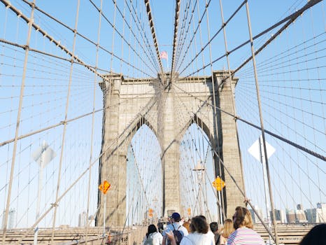 View of pedestrians walking on the Brooklyn Bridge, capturing its iconic architecture against a clear sky.