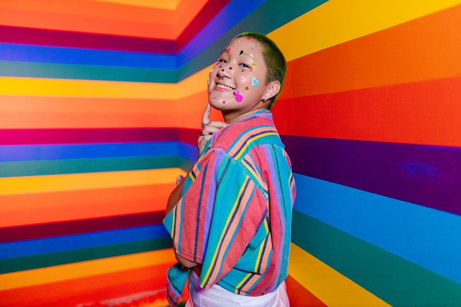 Smiling woman with face stickers in a vibrant, striped room.