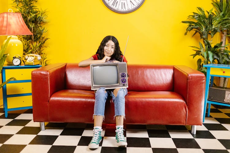 A Woman Sitting On The Couch While Holding A TV