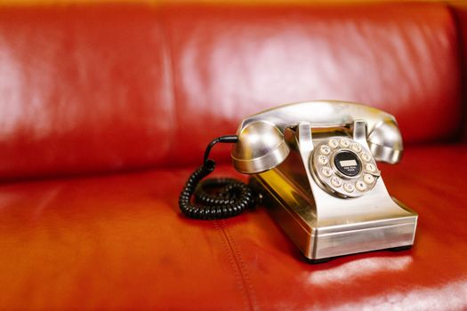 Close-up of a classic rotary phone on a red leather chair, evoking nostalgia.