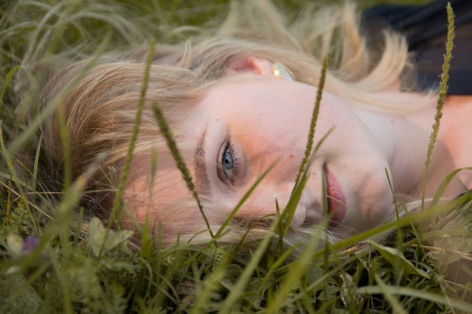 Close-up of a woman lying peacefully on grass, surrounded by nature.