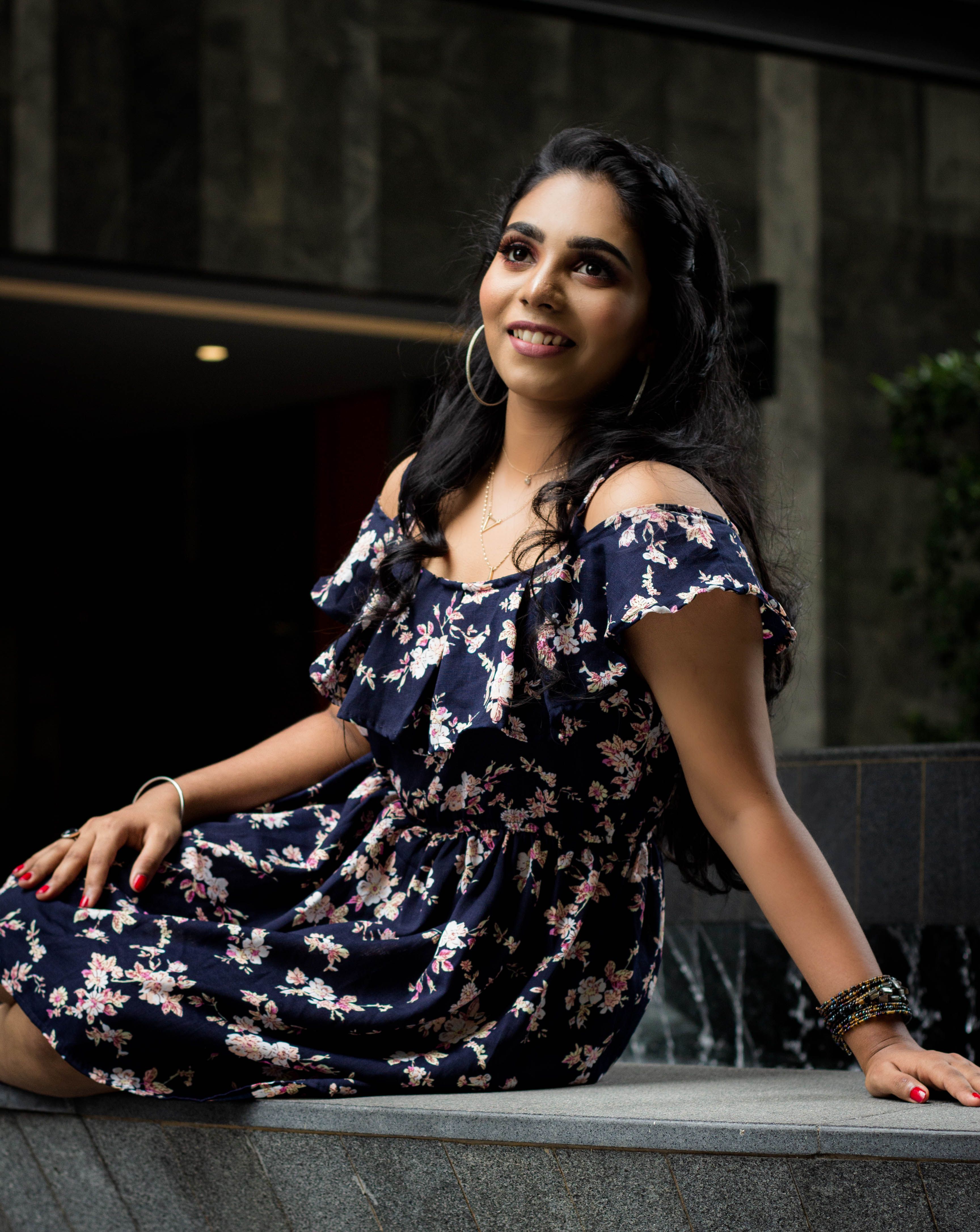 A smiling woman wearing a floral dress sits outdoors in Kuala Lumpur, Malaysia.