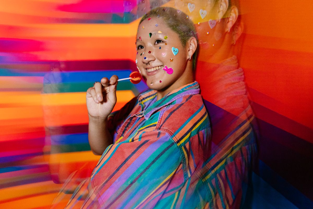 Colorful portrait featuring a smiling person with rainbow stickers and lollipop, expressing joy and diversity.
