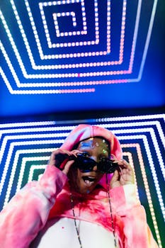 A stylish adult wearing sunglasses and a colorful hoodie at a neon-lit party.