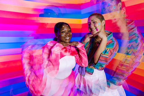 Free Two women posing playfully against a vivid rainbow backdrop, exuding happiness and creativity. Stock Photo